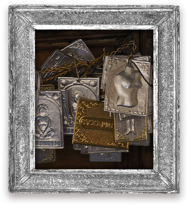 Old silver and brass milagro plaques, in a pressed-tin frame